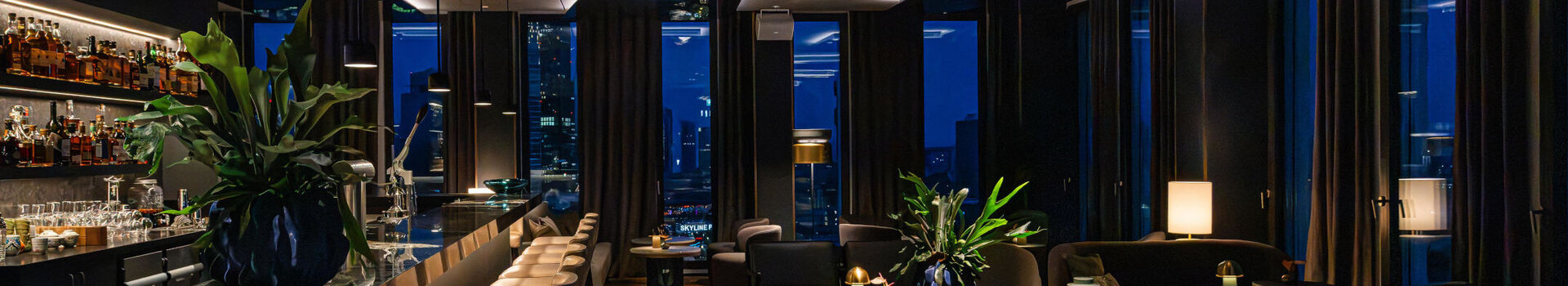Moderne Bar mit stimmungsvollem Ambiente und dunklen Möbeln sowie Ausblick auf die Frankfurter Skyline.
