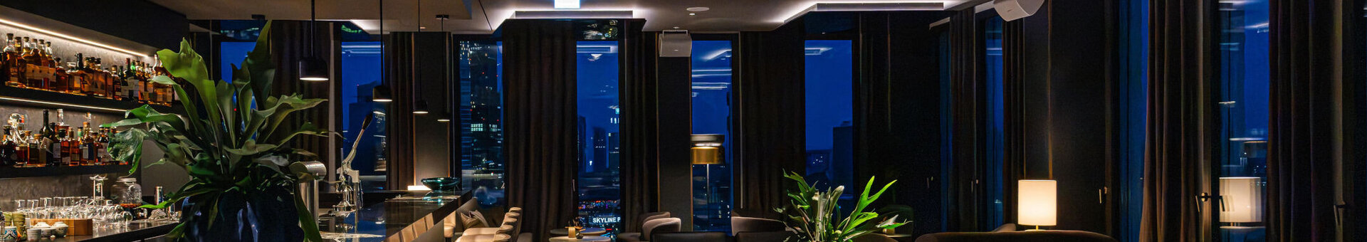 A modern bar with a cosy atmosphere, dark furniture and views of the Frankfurt skyline.