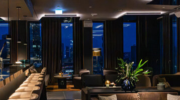 A modern bar with a cosy atmosphere, dark furniture and views of the Frankfurt skyline.