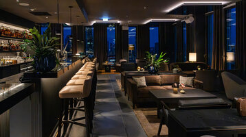 Moderne Bar mit stimmungsvollem Ambiente und dunklen Möbeln sowie Ausblick auf die Frankfurter Skyline.