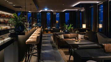 Moderne Bar mit stimmungsvollem Ambiente und dunklen Möbeln sowie Ausblick auf die Frankfurter Skyline.