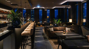 A modern bar with a cosy atmosphere, dark furniture and views of the Frankfurt skyline.