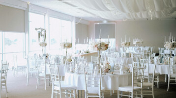 Elegant function room with white tables, flower arrangements and candles at the ATLANTIC Hotel Galopprennbahn.