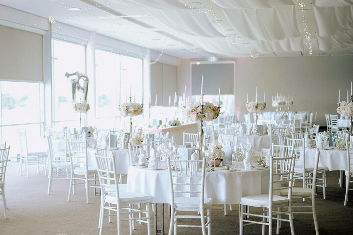 Elegant function room with white tables, flower arrangements and candles at the ATLANTIC Hotel Galopprennbahn.