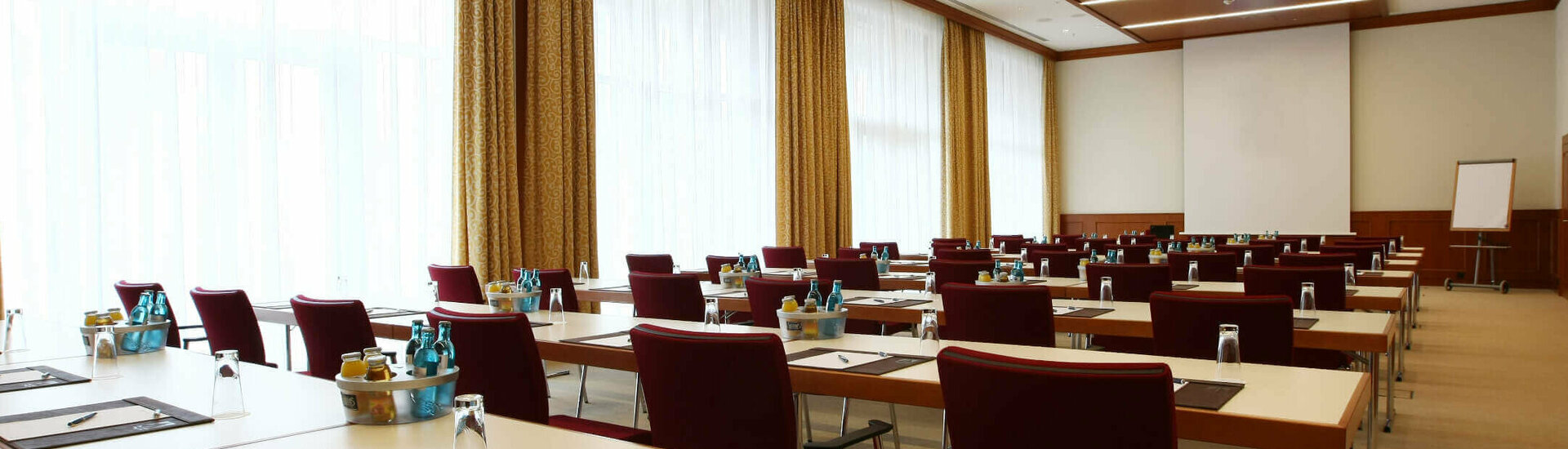 Modern conference room with rows of tables and chairs, equipped with writing utensils and drinks.