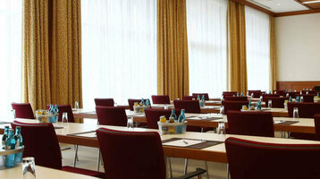 Moderner Konferenzraum mit Reihen von Tischen und Stühlen, ausgestattet mit Schreibutensilien und Getränken.