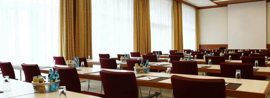 Moderner Konferenzraum mit Reihen von Tischen und Stühlen, ausgestattet mit Schreibutensilien und Getränken.