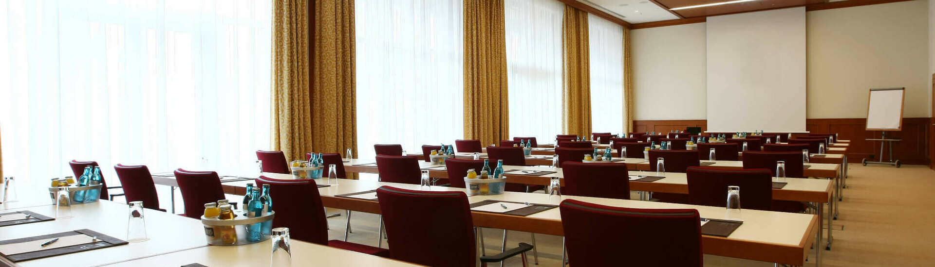 Veranstaltungsraum Bremen für Tagungen und Events Moderner Konferenzraum mit Reihen von Tischen und Stühlen, ausgestattet mit Schreibutensilien und Getränken.