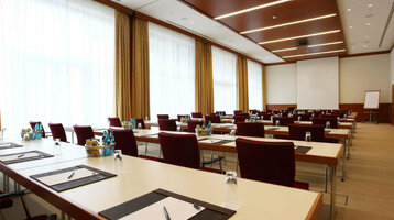 Function room Bremen for meetings and events Modern conference room with rows of tables and chairs, equipped with writing utensils and drinks.