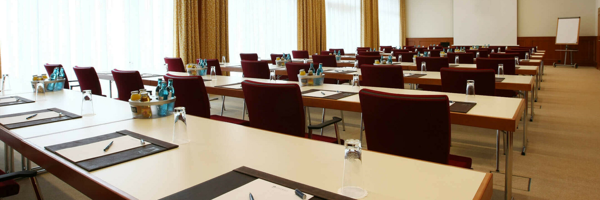 Moderner Konferenzraum mit Reihen von Tischen und Stühlen, ausgestattet mit Schreibutensilien und Getränken.