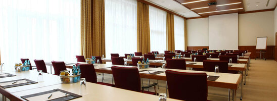 Modern conference room with rows of tables and chairs, equipped with writing utensils and drinks.