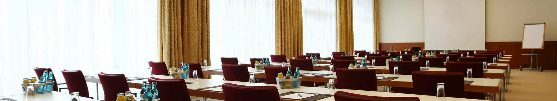 Moderner Konferenzraum mit Reihen von Tischen und Stühlen, ausgestattet mit Schreibutensilien und Getränken.