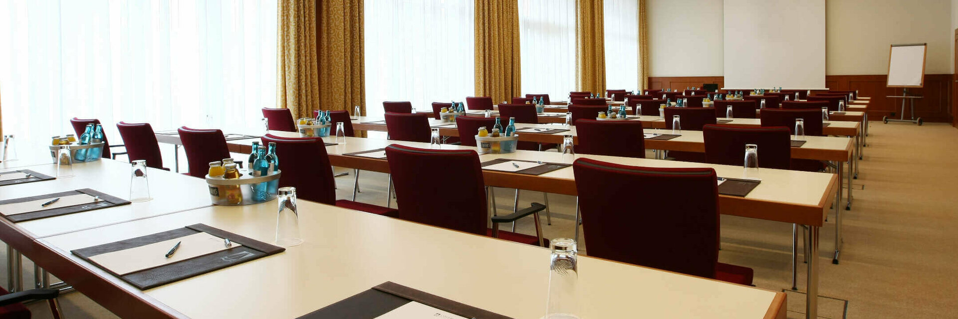 Modern conference room with rows of tables and chairs, equipped with writing utensils and drinks.