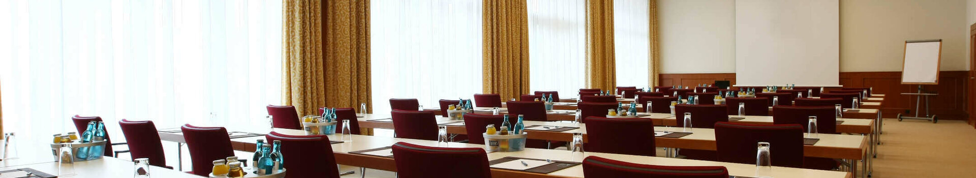 Modern conference room with rows of tables and chairs, equipped with writing utensils and drinks.
