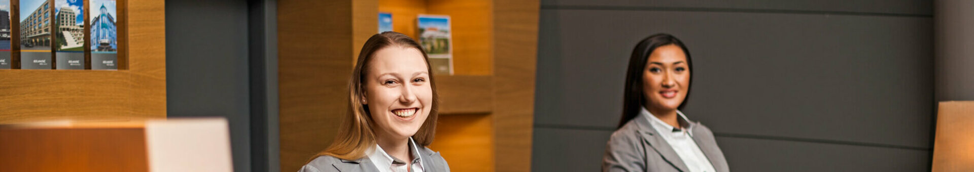 Reception in the ATLANTIC Hotel Airport in Bremen  Two receptionists in gray suits smile at the reception desk of the ATLANTIC Hotel Airport Bremen.