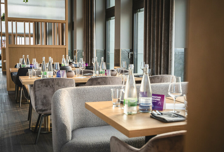 Elegantes Hotelrestaurant mit gedeckten Tischen, Wasserflaschen und Gläsern, in modernem, lichtdurchflutetem Ambiente.