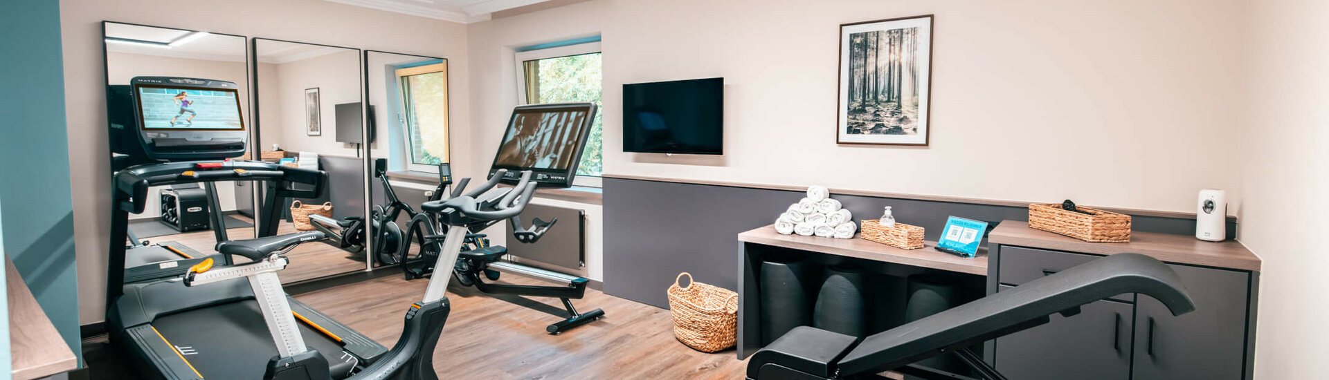Moderner Fitnessraum im ATLANTIC Hotel Landgut Horn Bremen mit Laufband, Heimtrainer, Spiegeln und Handtüchern.