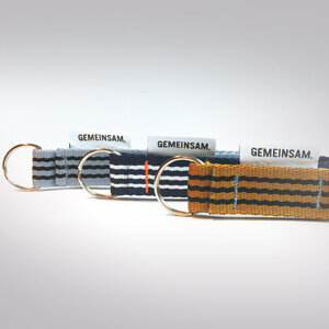 Four colorful key rings with the inscription "GEMEINSAM" lie next to each other on a bright surface.