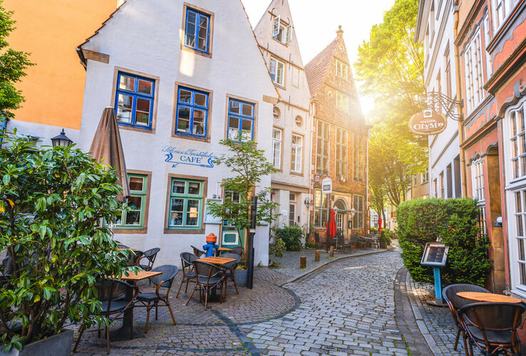 Picturesque old town alley in Bremen with historic buildings, café terrace and cobblestones in sunlight.