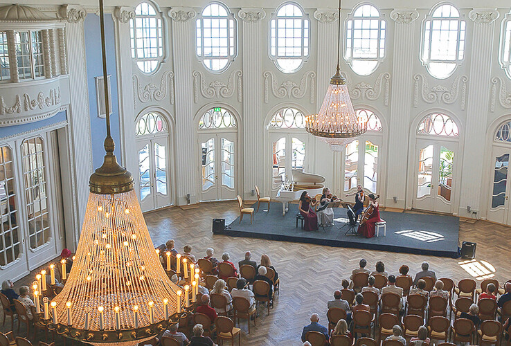 Elegant concert hall in the ATLANTIC Grand Hotel Travemünde with chandeliers and a string quartet on stage.