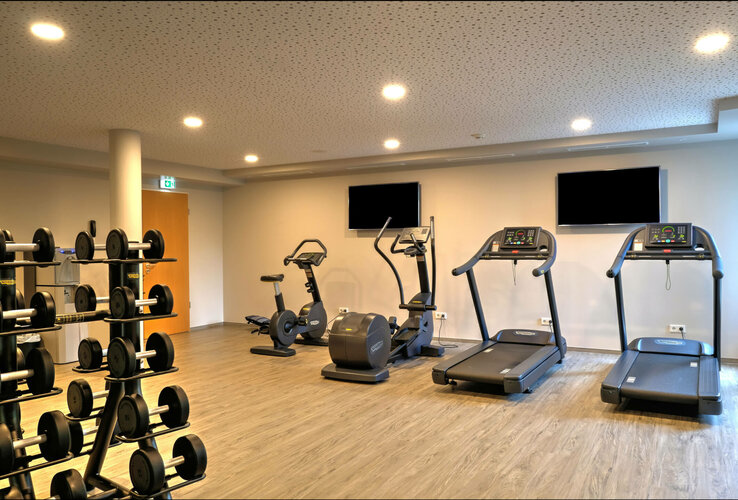 Bright fitness room with treadmills, bicycles and weights at the ATLANTIC Hotel Airport Bremen.