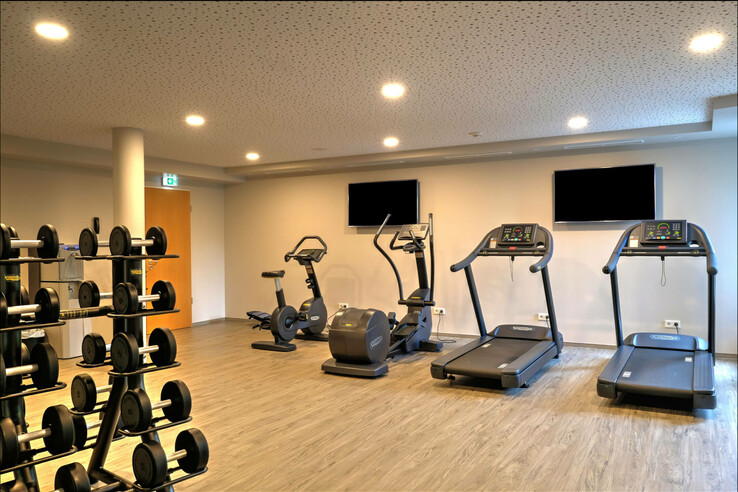 Bright fitness room with treadmills, bicycles and weights at the ATLANTIC Hotel Airport Bremen.