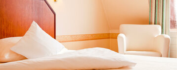 Bed and armchair in the room at the ATLANTIC Hotel Landgut Horn