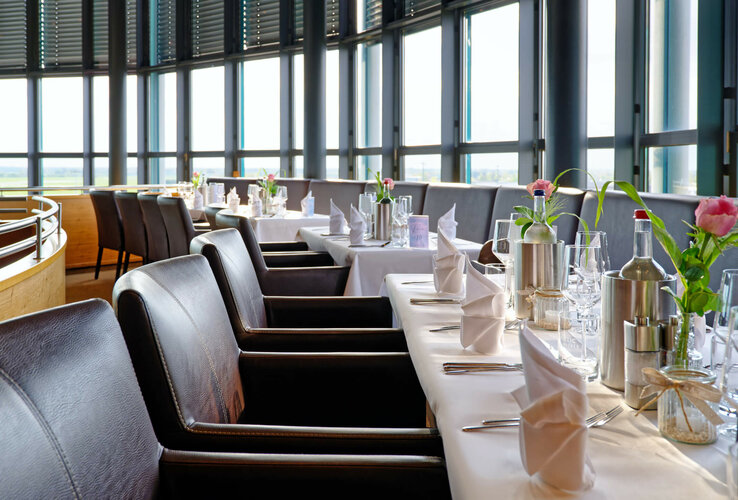 Elegantes Restaurant mit gedeckten Tischen, weißen Tischdecken, Ledersesseln und Panoramafenstern im ATLANTIC Hotel Airport.