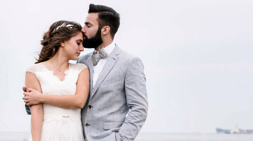 Brautpaar am Strand, umarmt sich in hohen Gräsern mit Meerblick im Hintergrund.