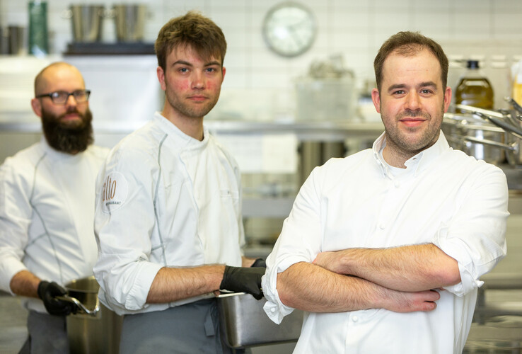 Three chefs in white chef's clothing stand in the kitchen of the ATLANTIC Grand Hotel Bremen.