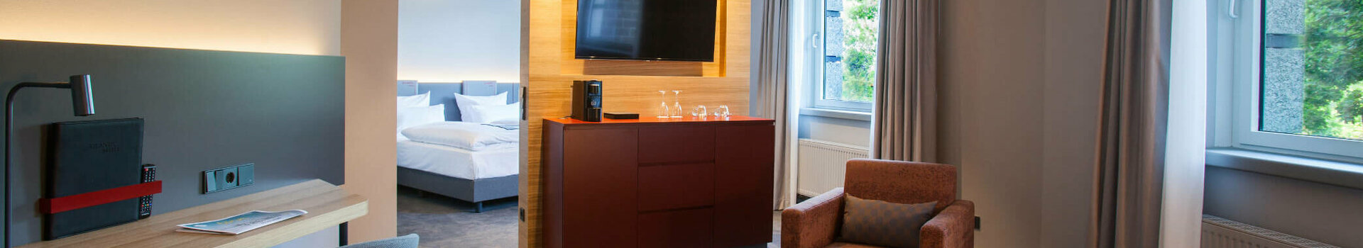 ATLANTIC Hotel Airport Bremen Suite Piccard Modern hotel room with seating area, desk, TV, large window and view of the bedroom at the ATLANTIC Hotel Airport.