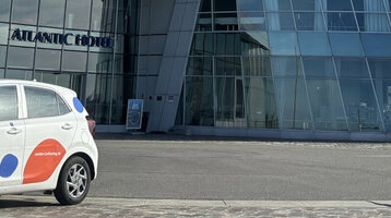 Ein weißer Kia Rio mit cambio-Logo steht vor dem ATLANTIC Hotel Sail City