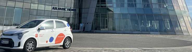 Ein weißer Kia Rio mit cambio-Logo steht vor dem ATLANTIC Hotel Sail City