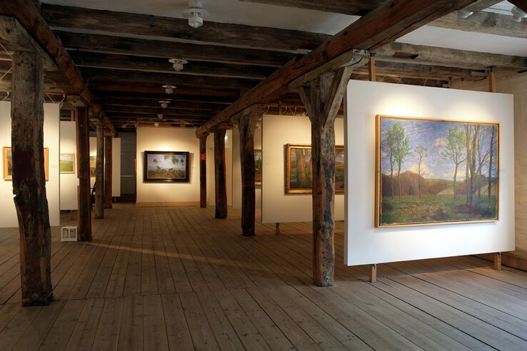Kunstgalerie mit Holzbalken, hölzernem Boden und Landschaftsgemälden an weißen Wänden im Overbeck Museum.