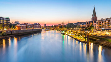 View of the Weser in Bremen at sunset, illuminated promenade and historic ships in the foreground.