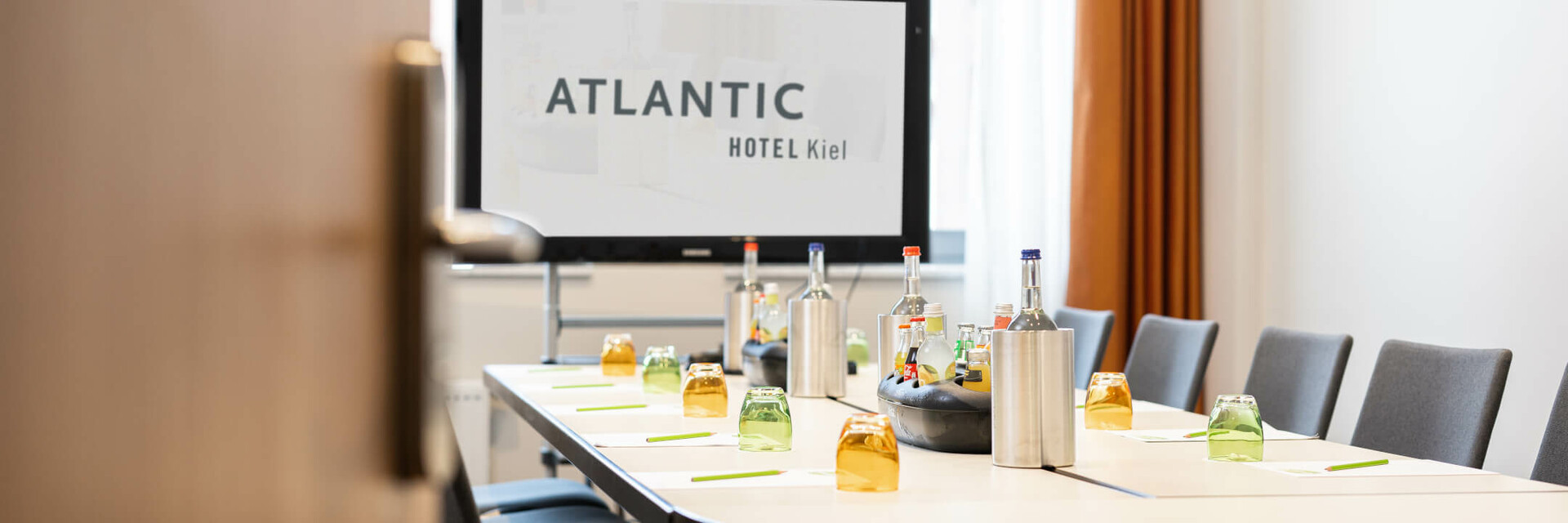 Moderner Konferenzraum im ATLANTIC Hotel Kiel mit gedecktem Tisch und Präsentationsbildschirm.