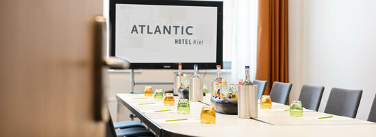 Modern conference room at the ATLANTIC Hotel Kiel with a set table and presentation screen.