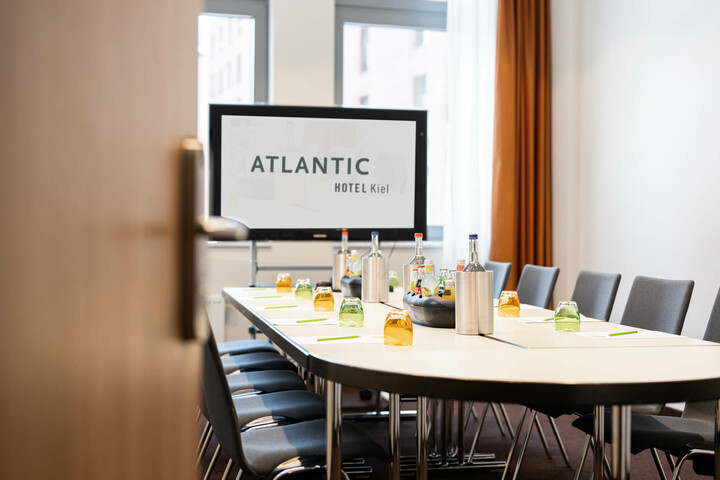 Moderner Konferenzraum im ATLANTIC Hotel Kiel mit gedecktem Tisch und Präsentationsbildschirm.