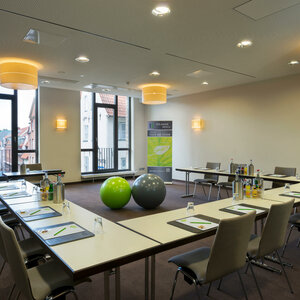 Moderner Konferenzraum im ATLANTIC Hotel Lübeck mit U-förmiger Bestuhlung, Flipchart und zwei bunten Gymnastikbällen.