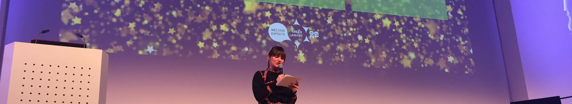 A woman gives a presentation on a stage with projected texts about the ATLANTIC Hotel Sail City in Bremerhaven.