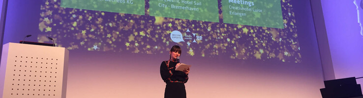Eine Frau hält eine Präsentation auf einer Bühne mit projizierten Texten zum ATLANTIC Hotel Sail City in Bremerhaven.