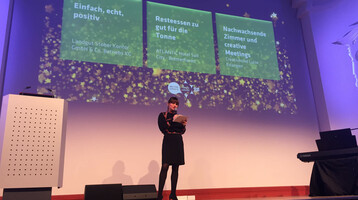 GCB-Award Verleihung in Leipzig Februar 2019 Eine Frau hält eine Präsentation auf einer Bühne mit projizierten Texten zum ATLANTIC Hotel Sail City in Bremerhaven.