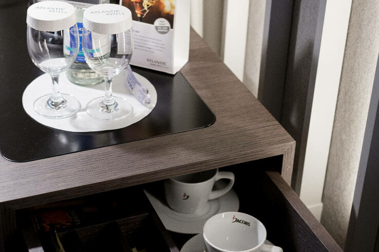 Minibar in the ATLANTIC Grand Hotel Bremen with glasses, cups, water bottle and tea selection.