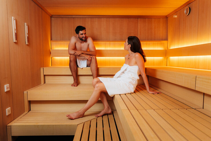 Zwei Personen entspannen in einer modernen, holzvertäfelten Sauna des ATLANTIC Hotel Heidelberg.