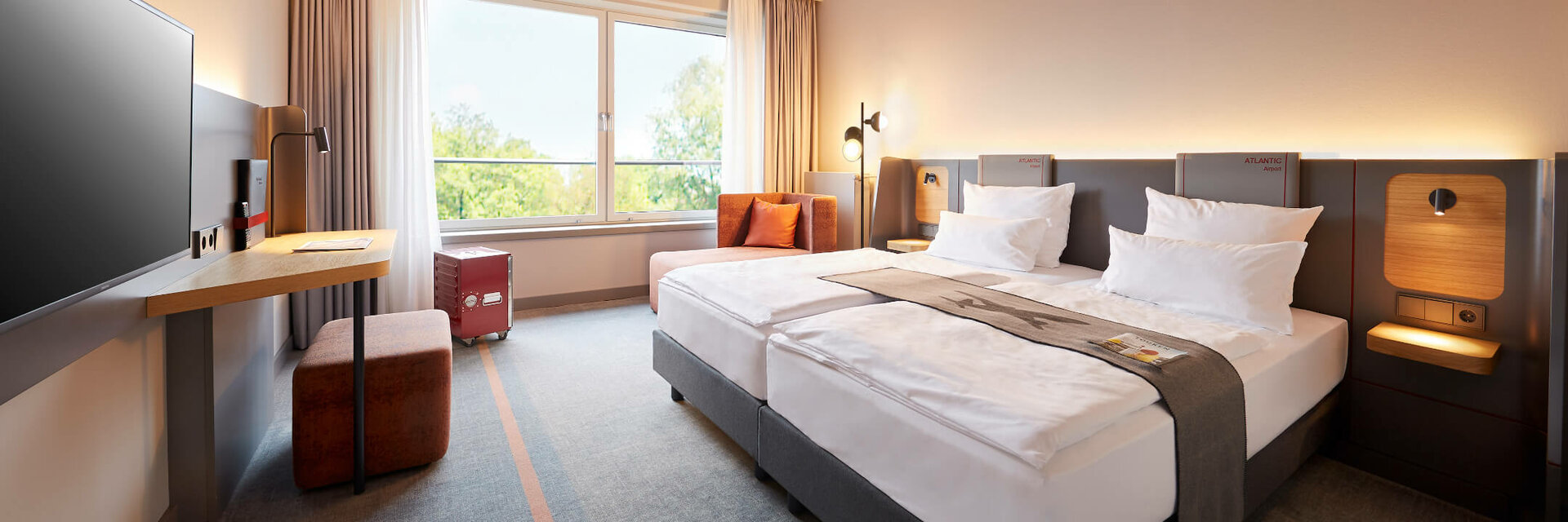 Modernes Hotelzimmer mit zwei Betten, großem Fenster, Schreibtisch und Himmelmotiv an der Decke im ATLANTIC Hotel Airport.