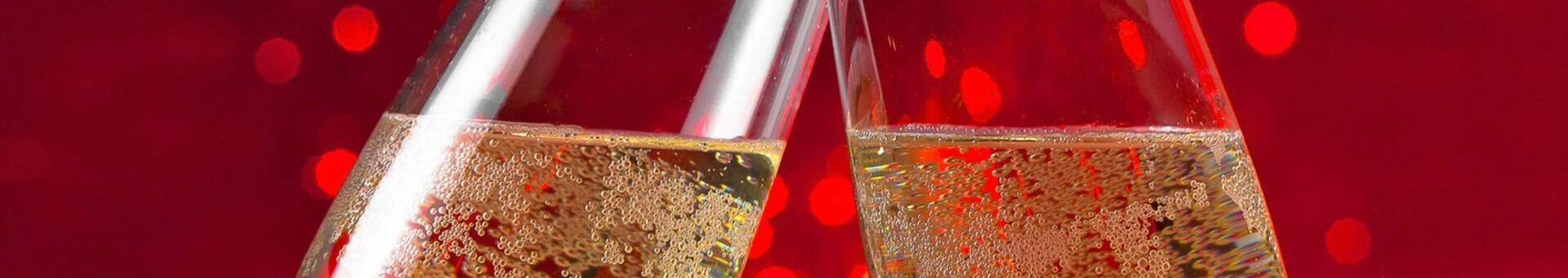 Zwei Sektgläser stoßen vor rotem, funkelndem Hintergrund an.
