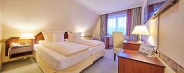 Bed, sitting area and television in the classic double room at the ATLANTIC Hotel Landgut Horn