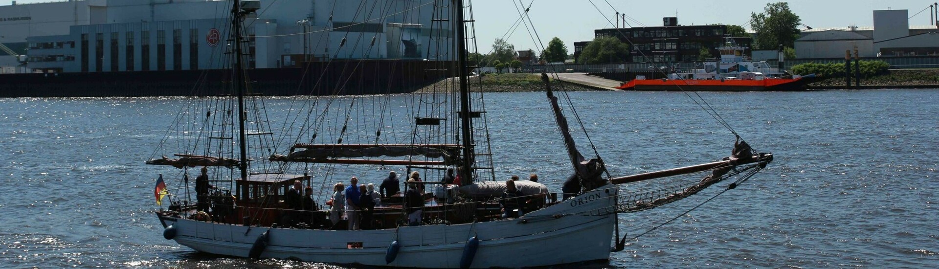 Sailing ship on the Weser against an industrial backdrop in Vegesack under a clear sky.