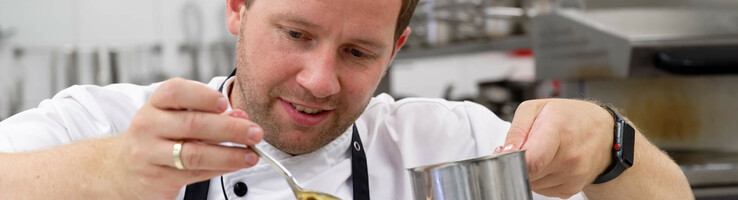 Koch verfeinert kunstvoll ein Gericht in der Küche des ATLANTIC Hotel Wilhelmshaven.