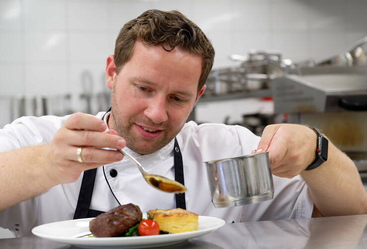 Koch verfeinert kunstvoll ein Gericht in der Küche des ATLANTIC Hotel Wilhelmshaven.